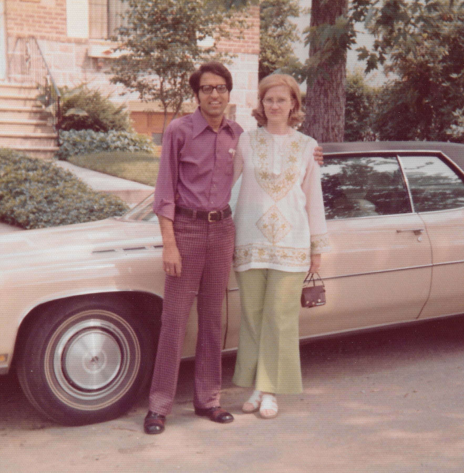 Madhu and Mary Lee standing beside a pale pink Buick outside a brick house