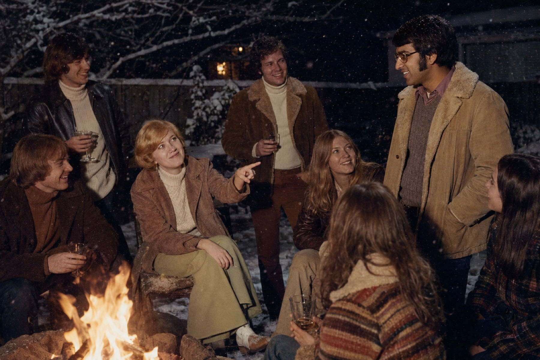 A circle of young people sitting around a campfire at dusk