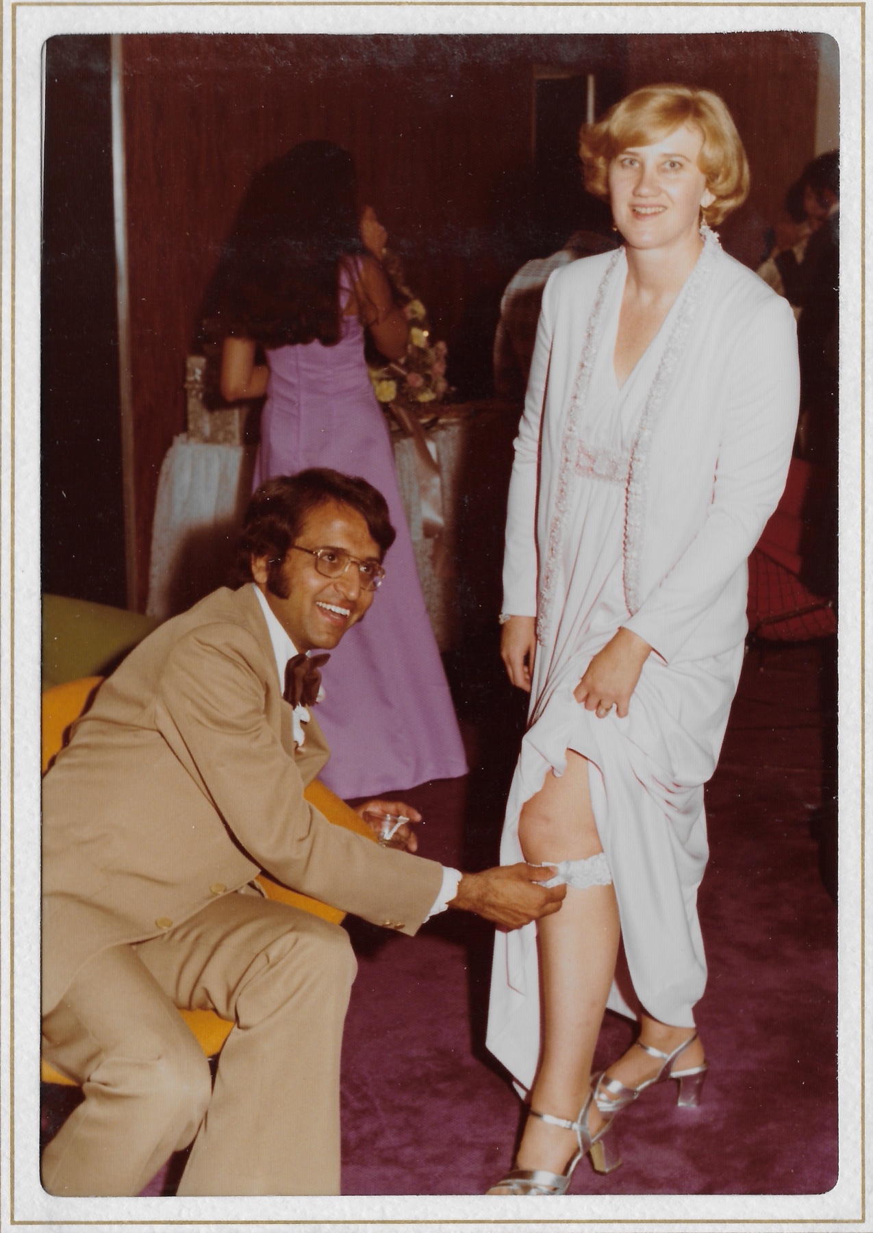 Madhu kneeling for the garter while Mary Lee laughs