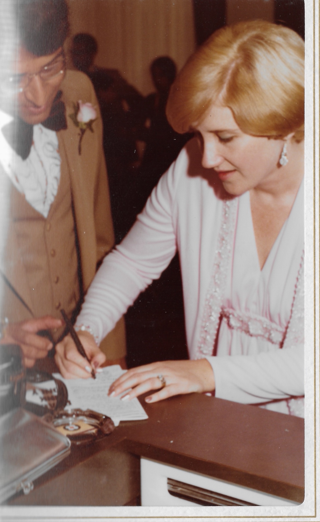 Mary Lee signing the marriage document while Madhu leans in to watch